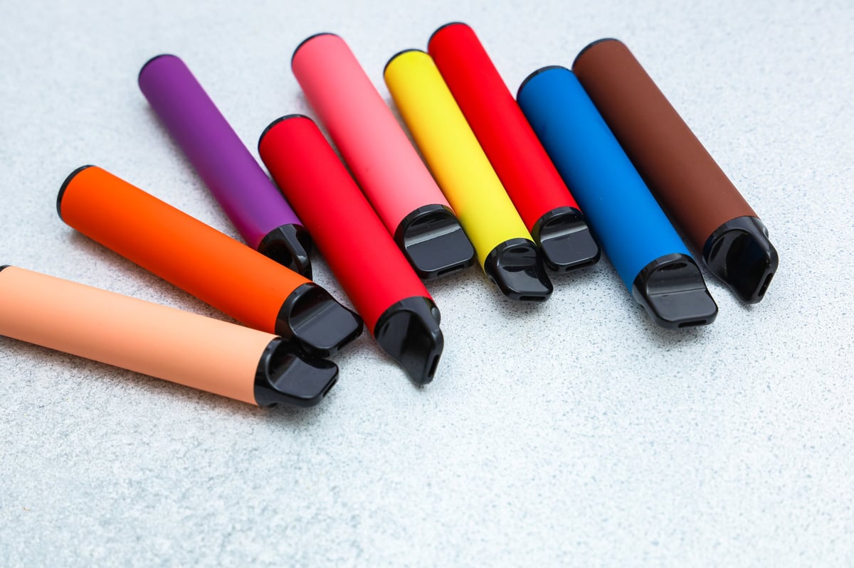 Vape pens in different colours arranged neatly on a grey surface