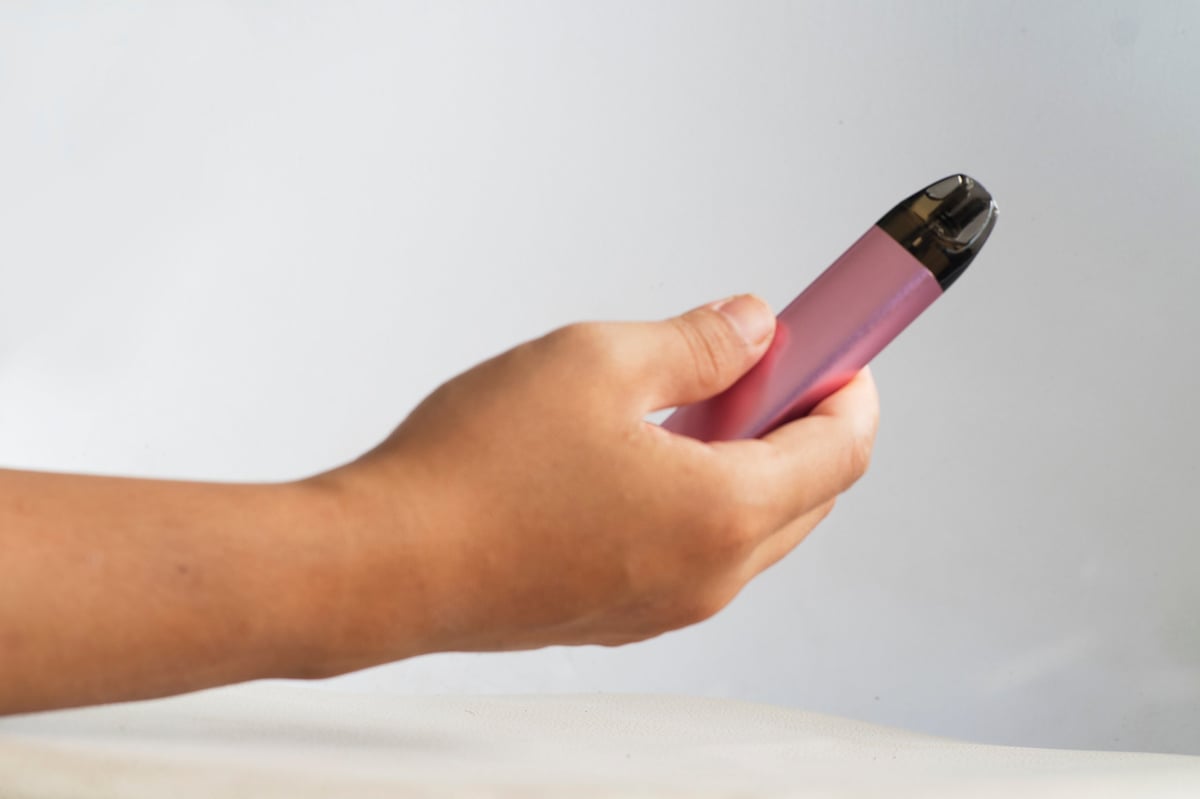Hand holding a disposable vape device with a digital display, on a white background