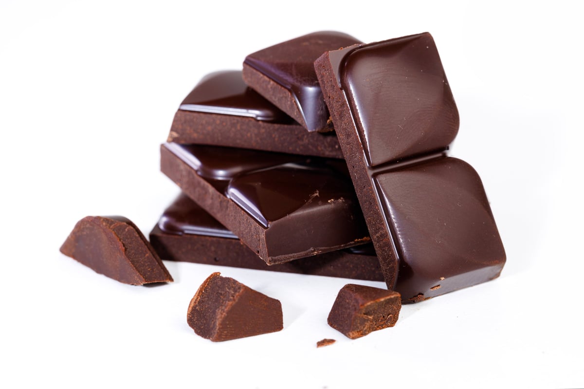 Cubes of dark chocolate broken from a bar on a white background