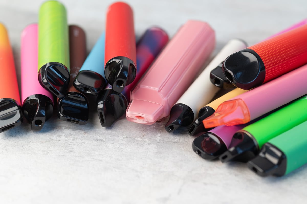 Collection of colourful disposable vape devices scattered on a light surface