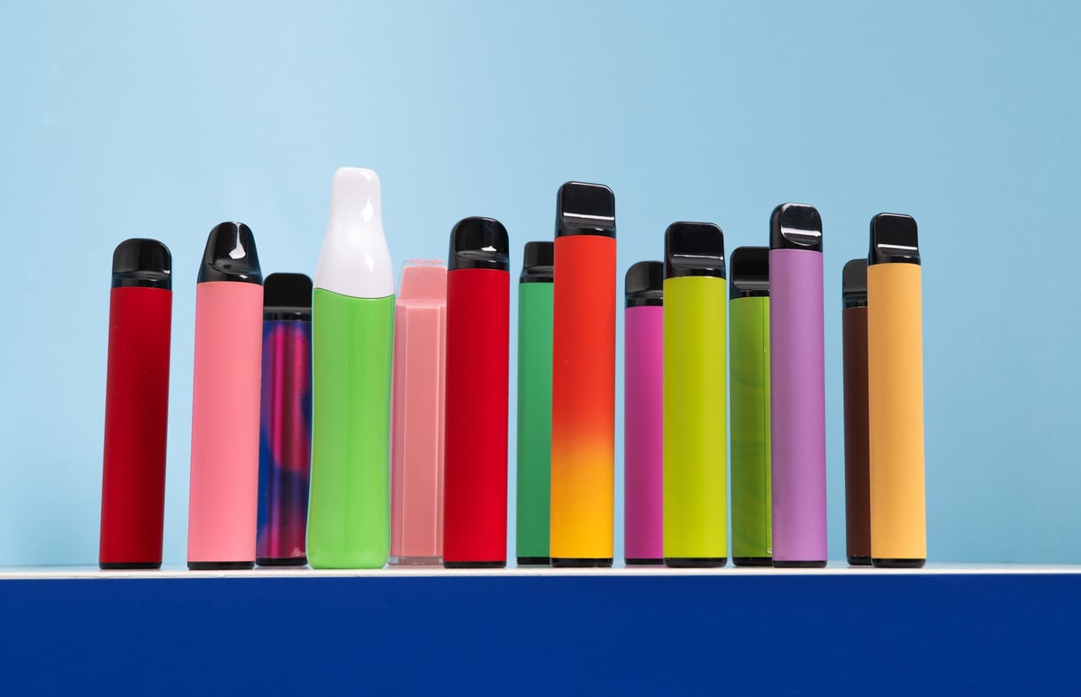 A range of colourful disposable vape pens lined up against a light blue background