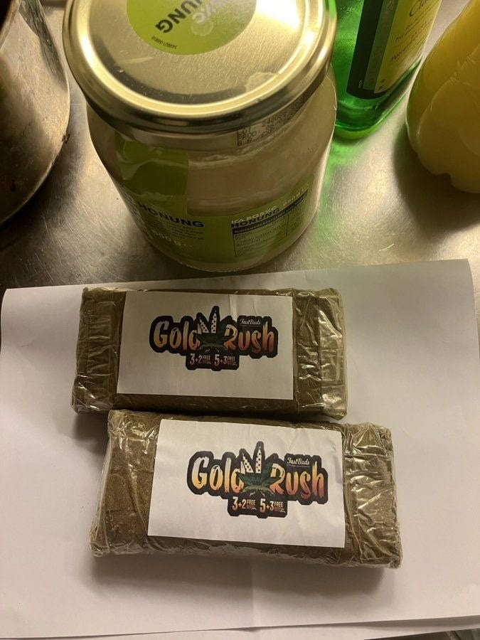 Two Gold Rush branded hash bars wrapped in gold foil on white paper, with jars in the background