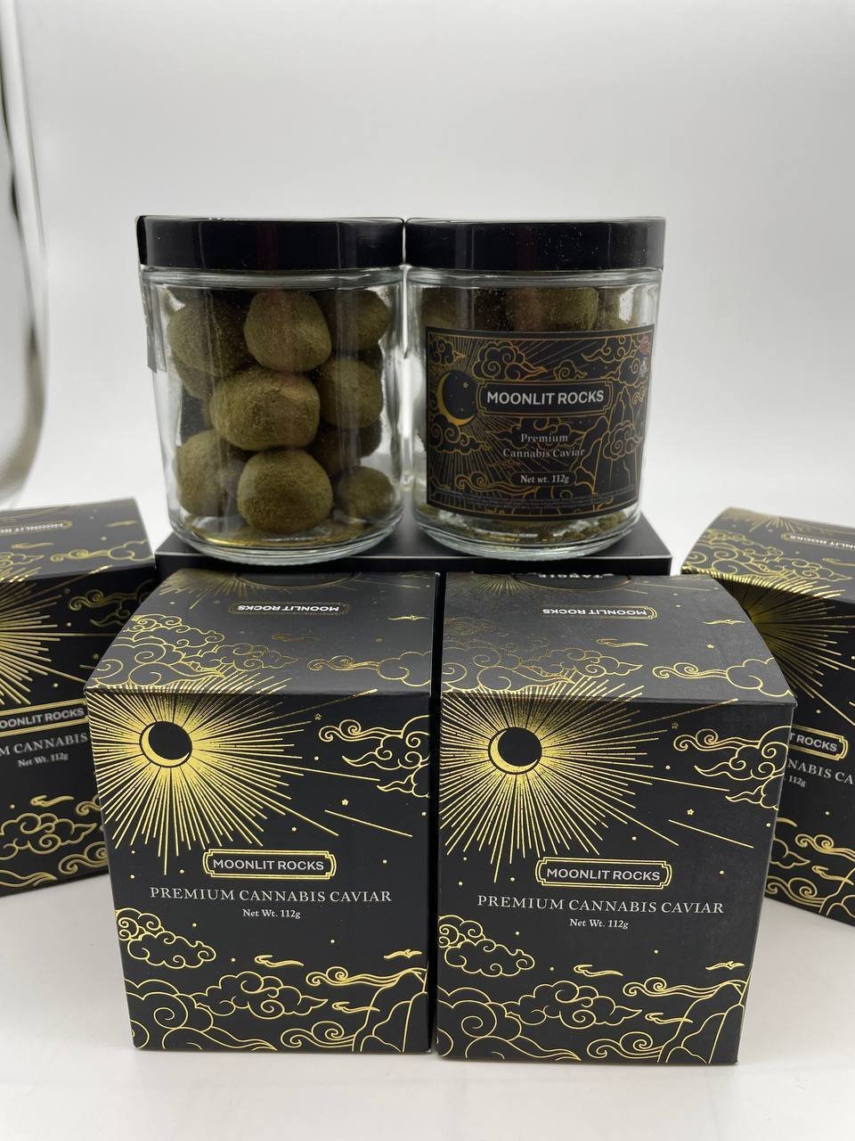 Two glass jars of Moonlit Rocks premium cannabis caviar with black lids beside the branded black and gold presentation boxes