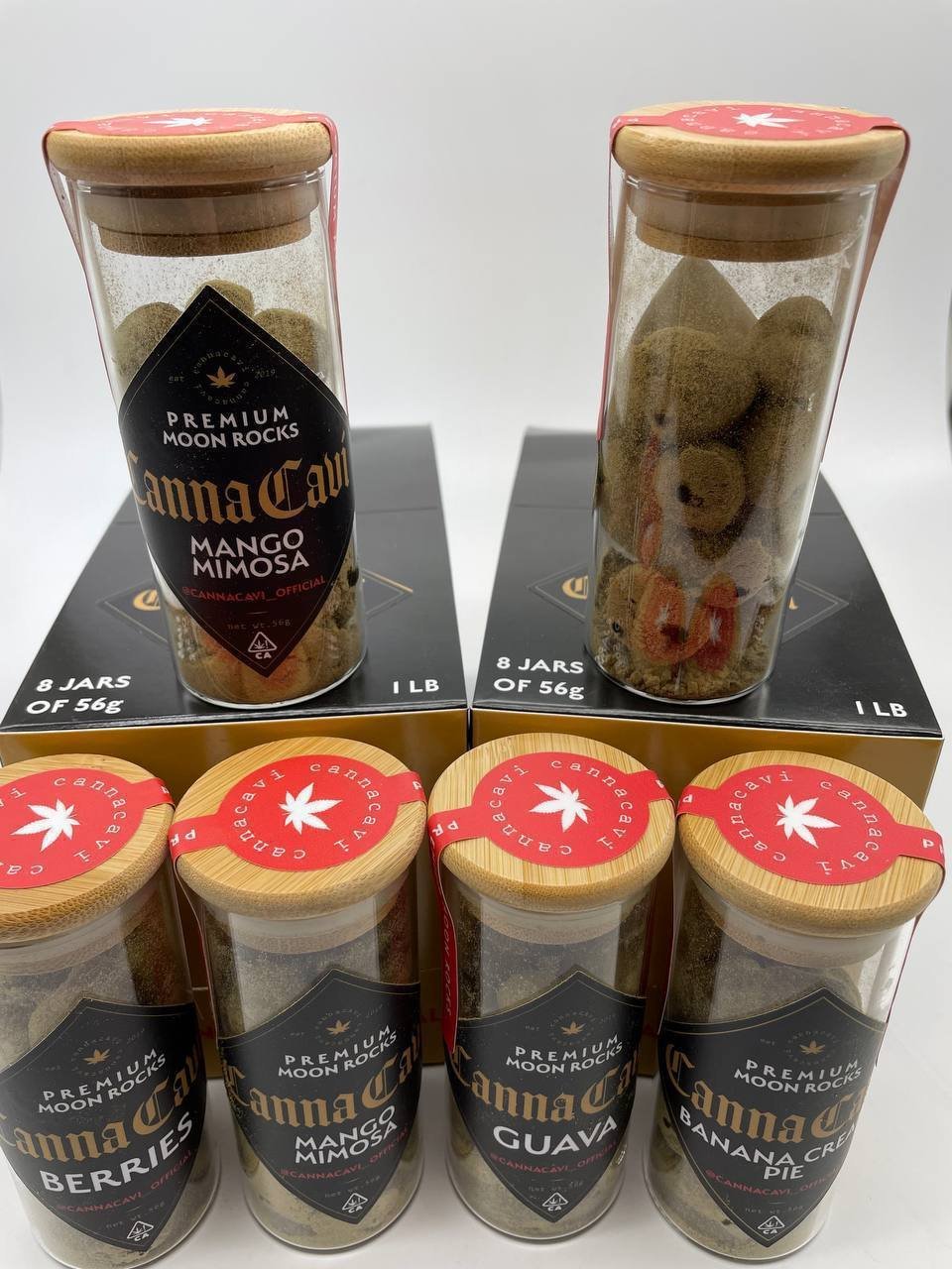 Six glass jars of Canna Cavi premium moon rocks with wooden lids and red seals, displayed on the branded black presentation boxes