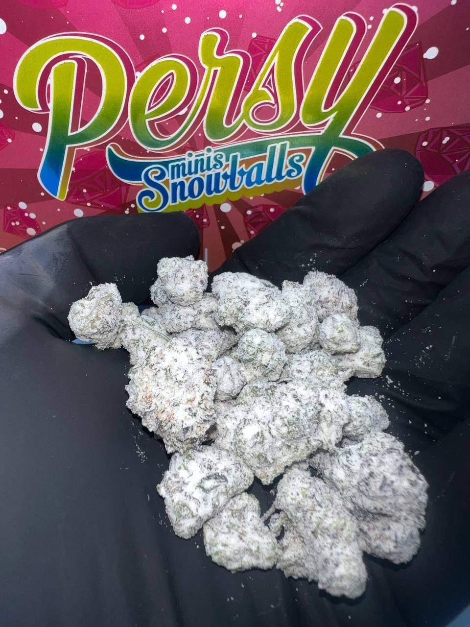 Hand holding Persy Mini Snowballs coated in white frosting against the pink Candy Edition packaging